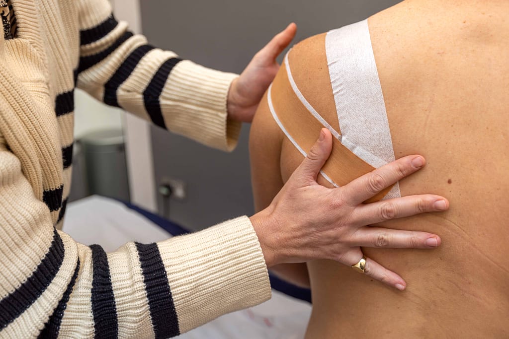 Physiotherapist applying tape to patient's shoulder